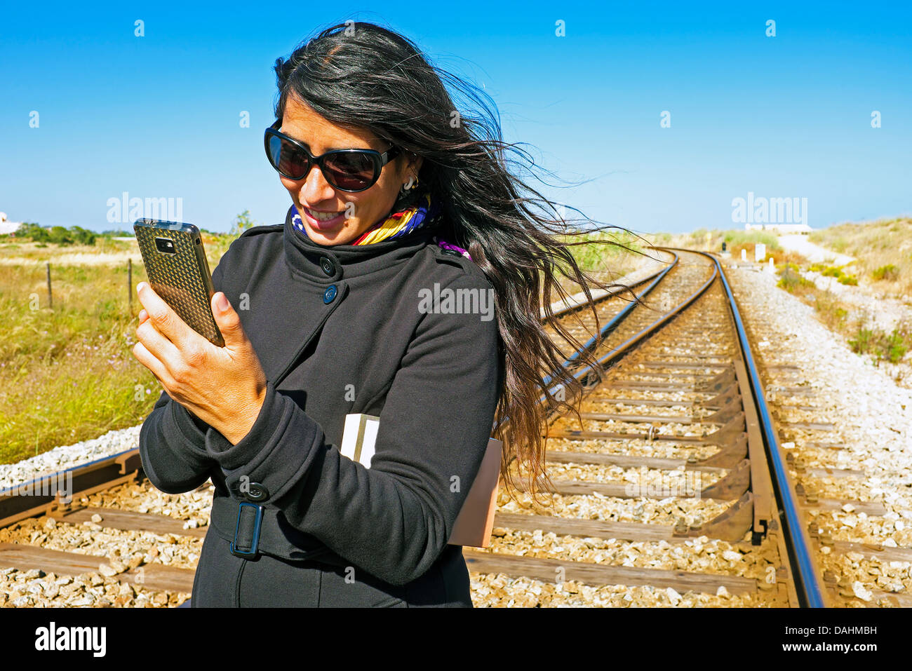 Junge schöne Frau schreibt eine SMS-Nachricht auf ein Bahngleis Stockfoto