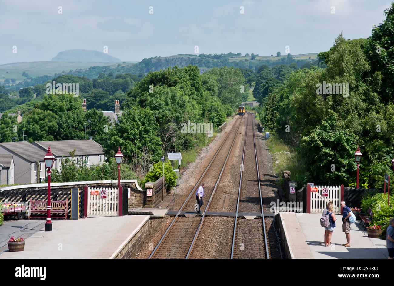 Ein Sprinter Personenzug fährt Station niederlassen, North Yorkshire, für Carlisle, Großbritannien gebunden. Ingleborough Hügel sichtbar am Horizont. Stockfoto