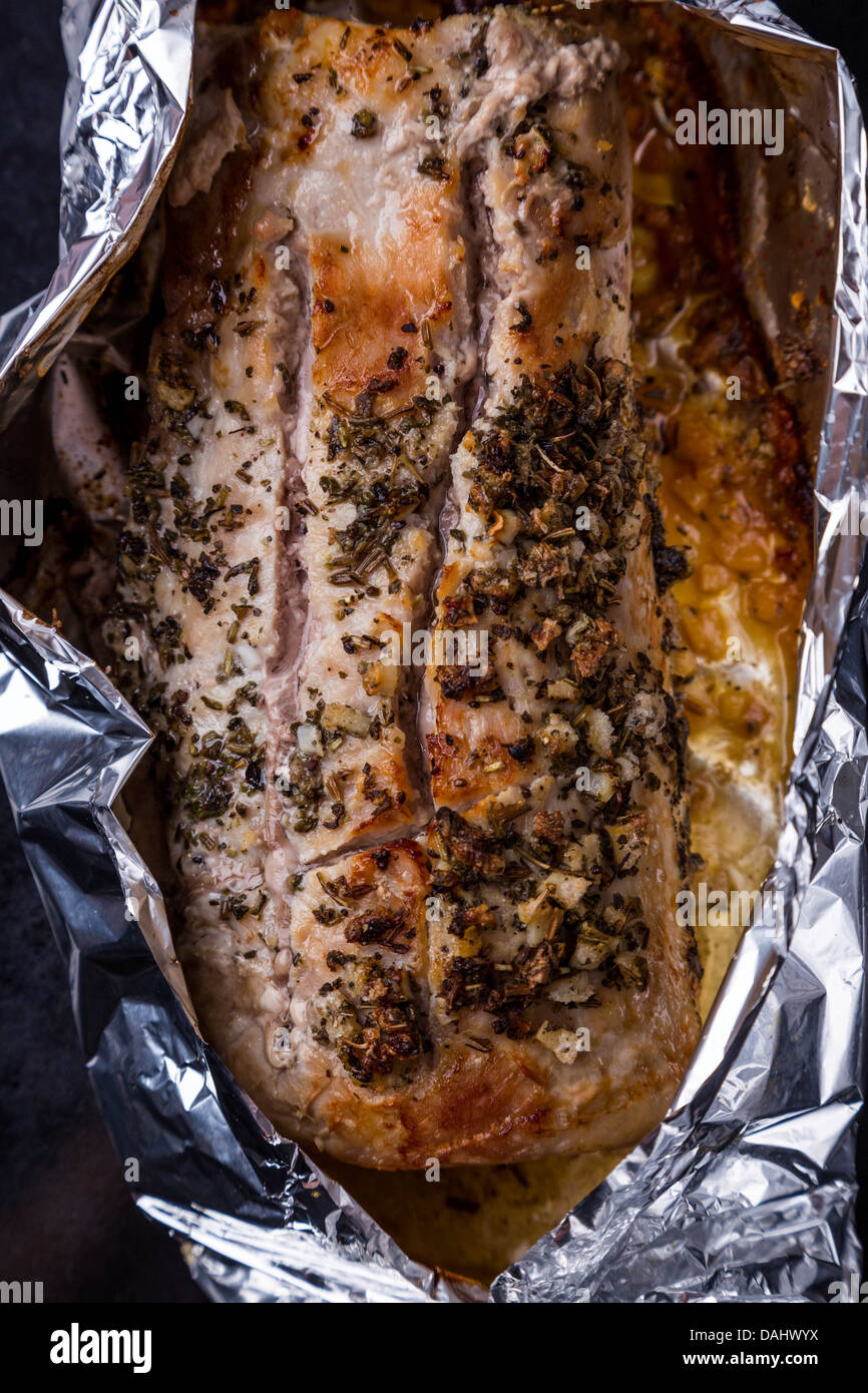 gebackenes Schweinefleisch mit Gewürzen in Alufolie auf schwarzen Tablett Stockfoto