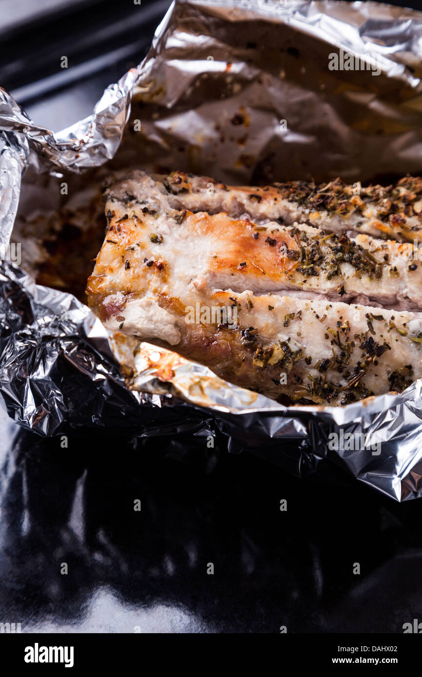 gebackenes Schweinefleisch mit Gewürzen in Alufolie auf schwarzen Tablett Stockfoto