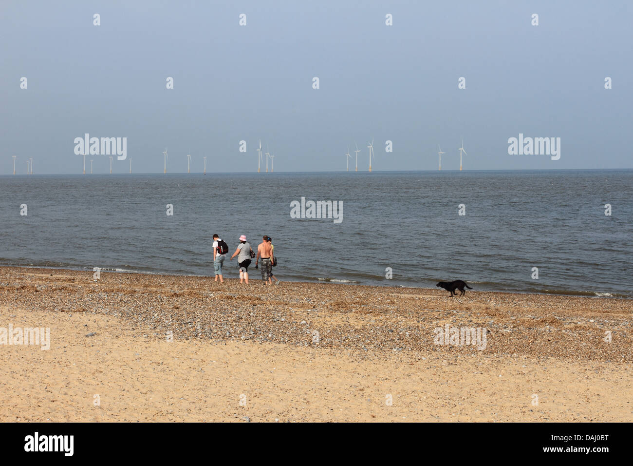 Leute laufen am Strand entlang, Urlauber genießen den Great Yarmouth Beach, Scroby Windkraftanlage hinten, Norfolk, Großbritannien Stockfoto