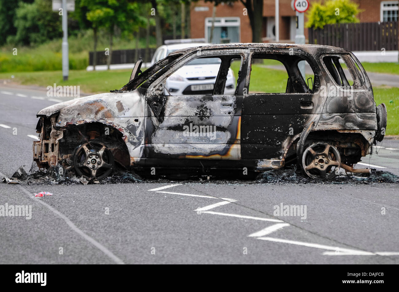 Newtownabbey, Nordirland. 15. Juli 2013 - sitzt A PSNI Polizeiauto hinter einem ausgebrannten Auto nach Ausschreitungen in Newtownabbey Stockfoto