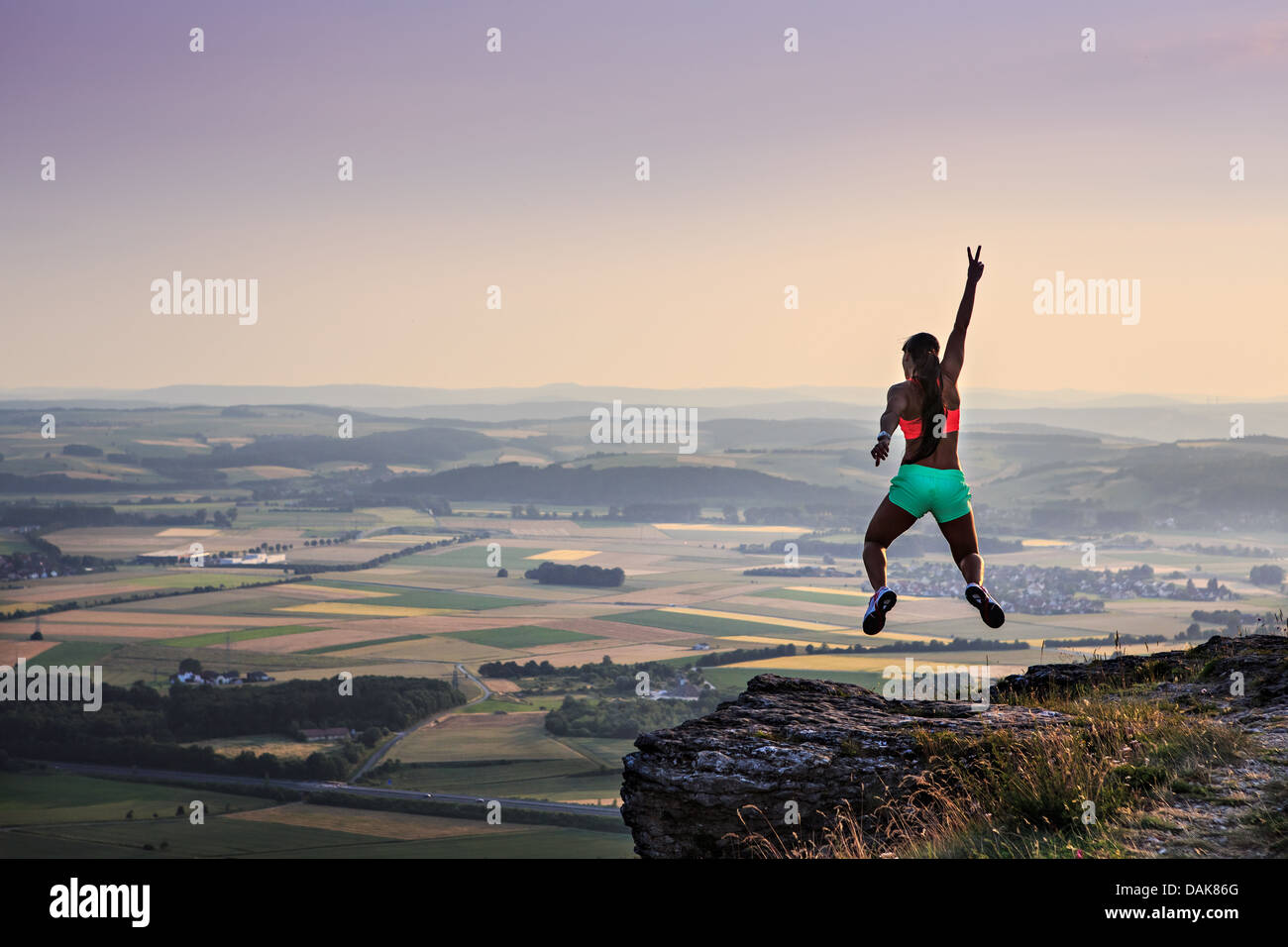 junge Frau springt auf einen Felsen vor ländliche Landschaft und Sonnenuntergang Stockfoto