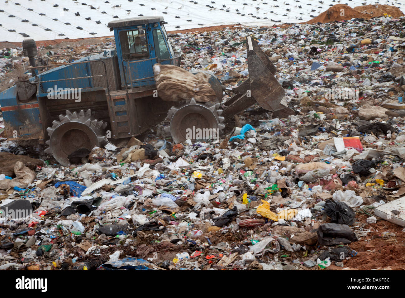 Müll türmt sich in Deponie jeden Tag während LKW mit Sand für sanitäre Zwecke abdeckt. Stockfoto