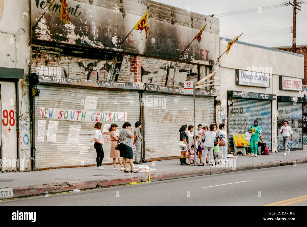 Multiethnische einheimischen warten auf einen Bus vor Brand beschädigt Geschäften in South Central Los Angeles nach 1992 Rodney King Riot. Stockfoto
