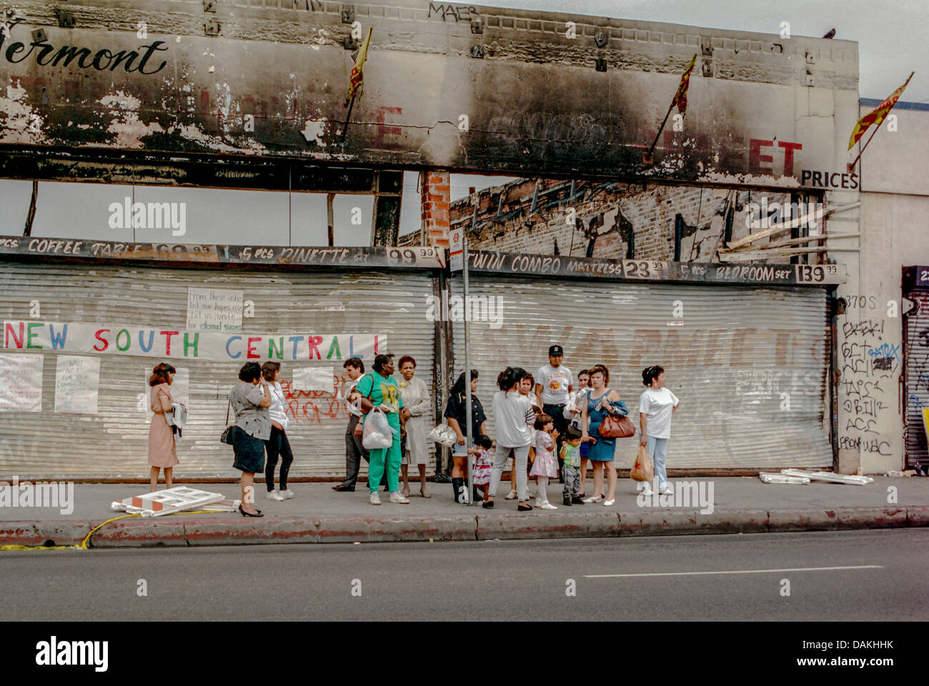 Multiethnische einheimischen warten auf einen Bus vor Brand beschädigt Geschäften in South Central Los Angeles nach 1992 Rodney King Race Riot. Stockfoto