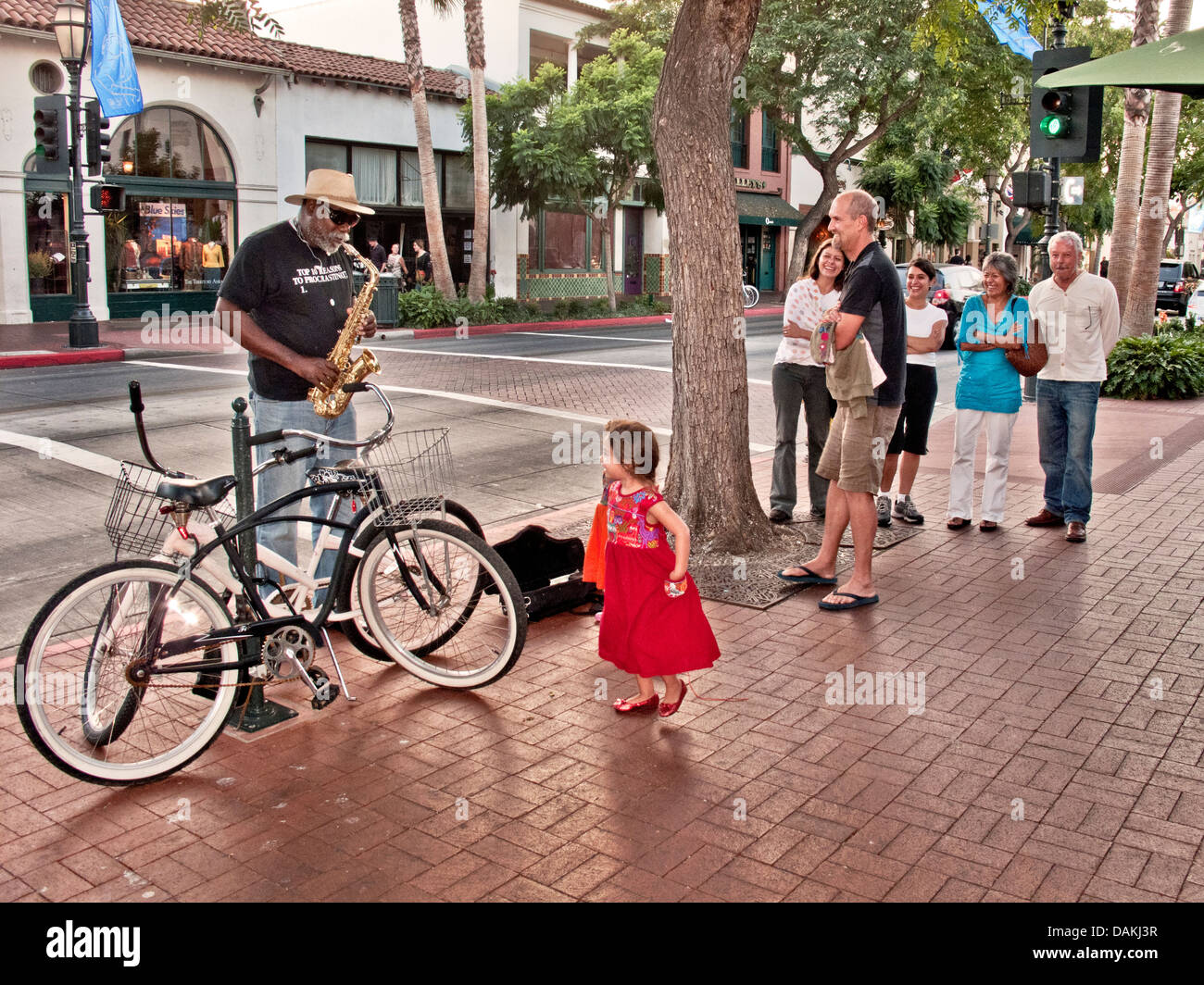 Zwei kleine Mädchen sind fasziniert von einer afroamerikanischen Bürgersteig Saxophonist auf der State Street in Santa Barbara, Kalifornien. Stockfoto