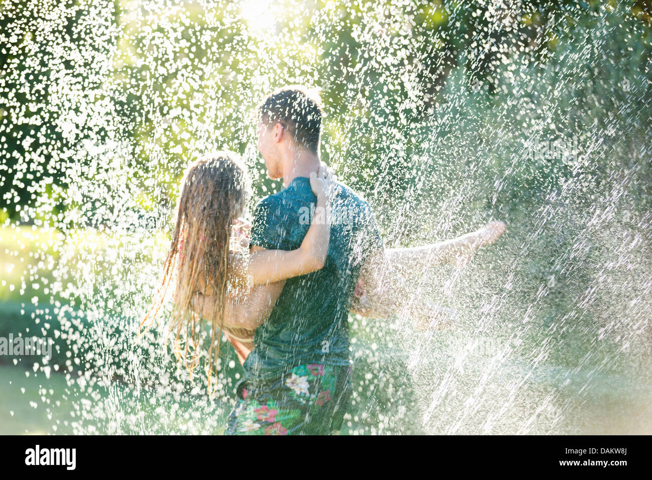 Paar im Sprinkler im Hinterhof spielen Stockfoto