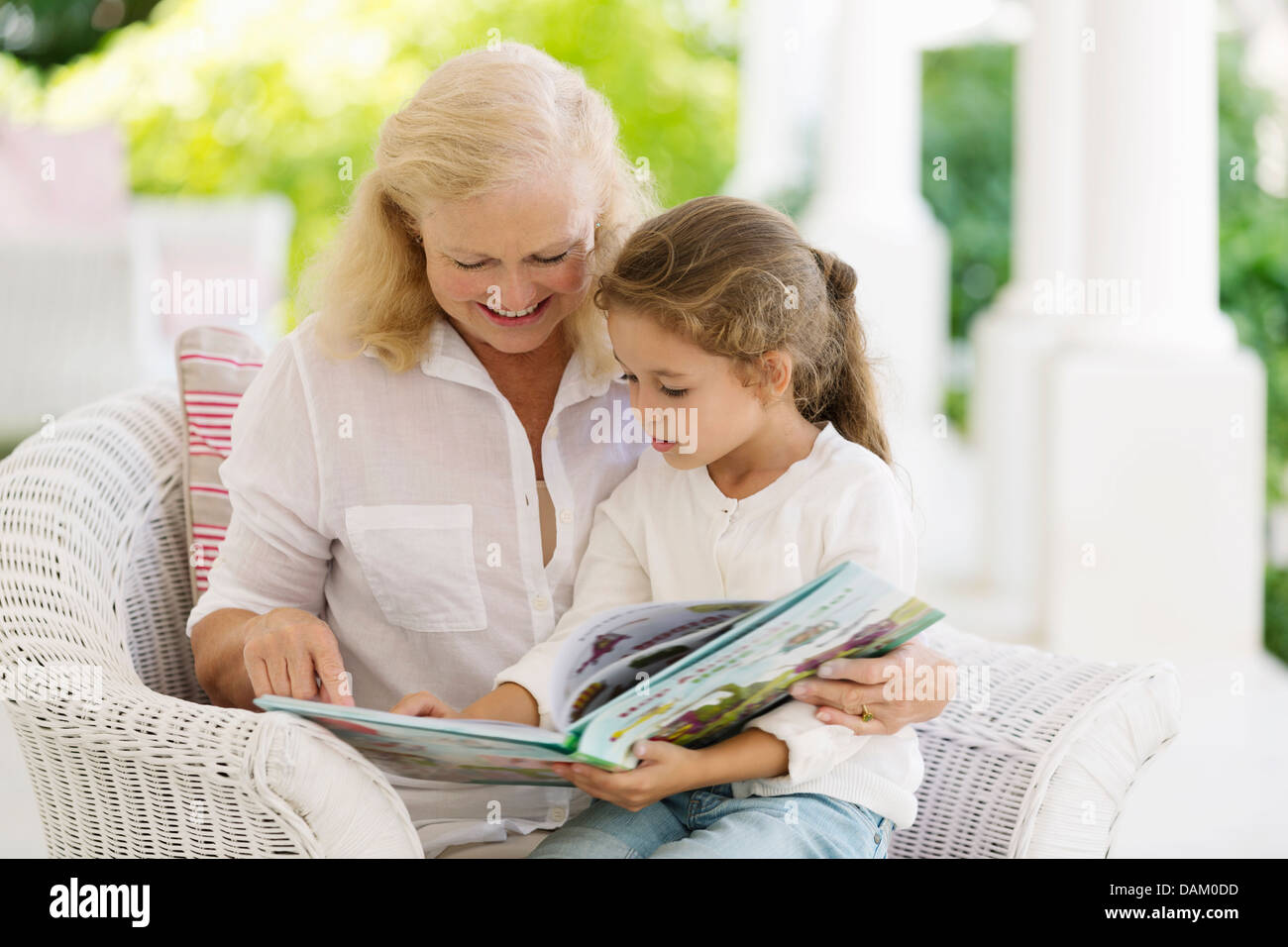 Ältere Frau liest Enkelin auf Veranda Stockfoto