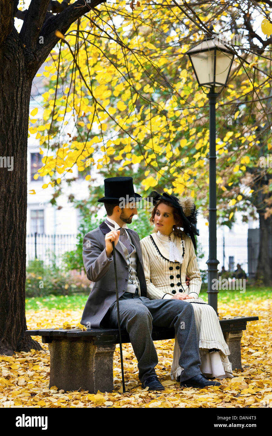 Ein Liebespaar, gekleidet im Stil am Ende des 19. Jahrhunderts, im Herbst auf einer Parkbank sitzen. Stockfoto