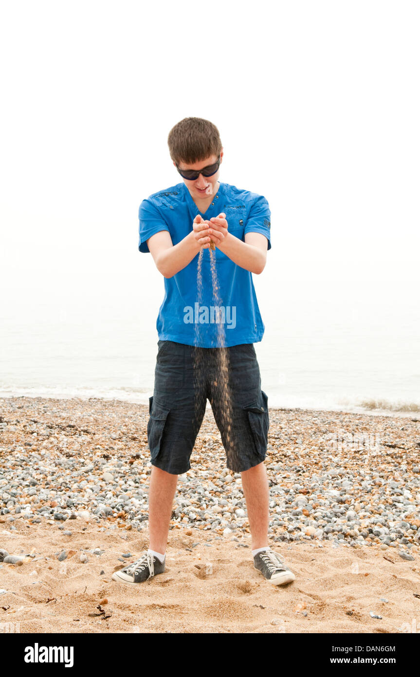 Ein junger Mann stehend an einem Strand und Sand durch die Finger laufen zu lassen Stockfoto