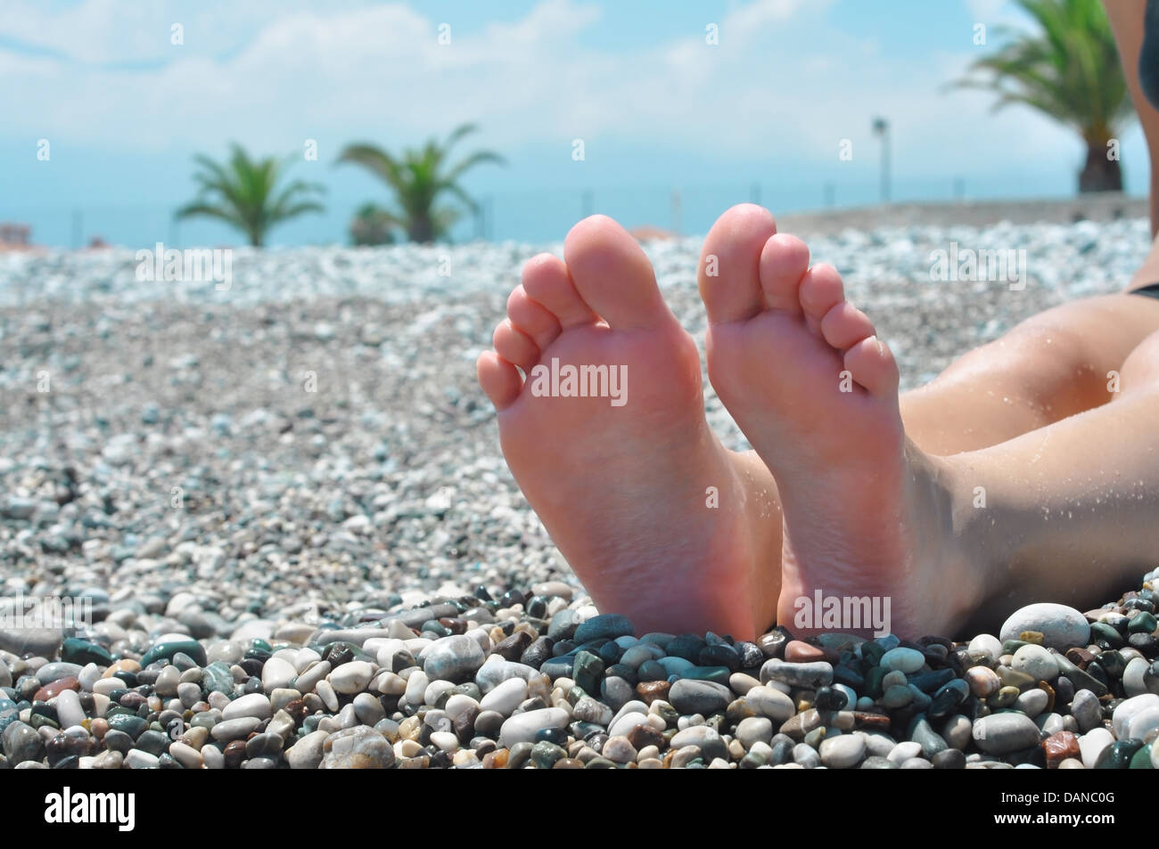 junge weibliche Füße am Strand von runden bunten Steinen Stockfoto