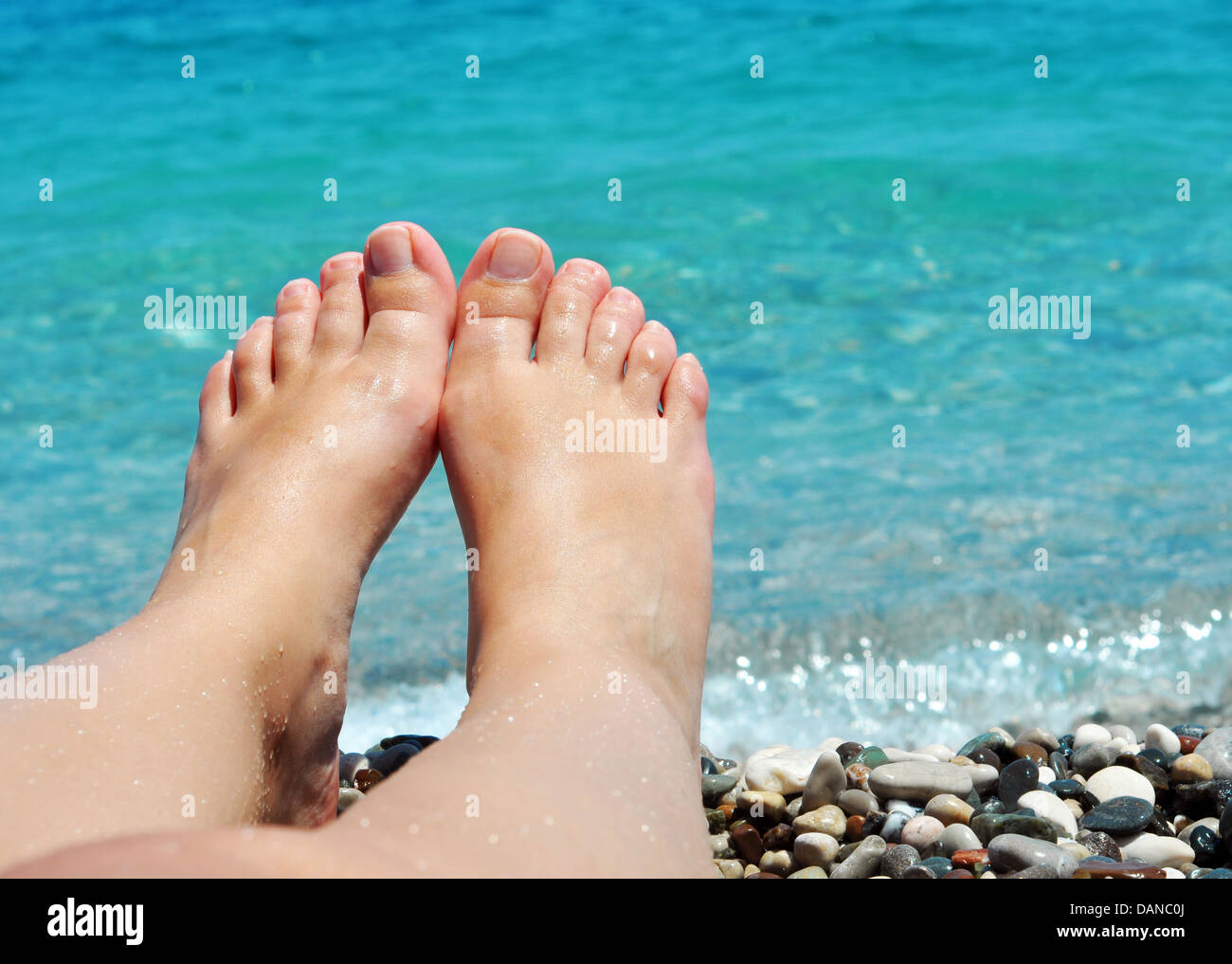 junge weibliche Füße am Strand mit blauem Wasser Stockfoto