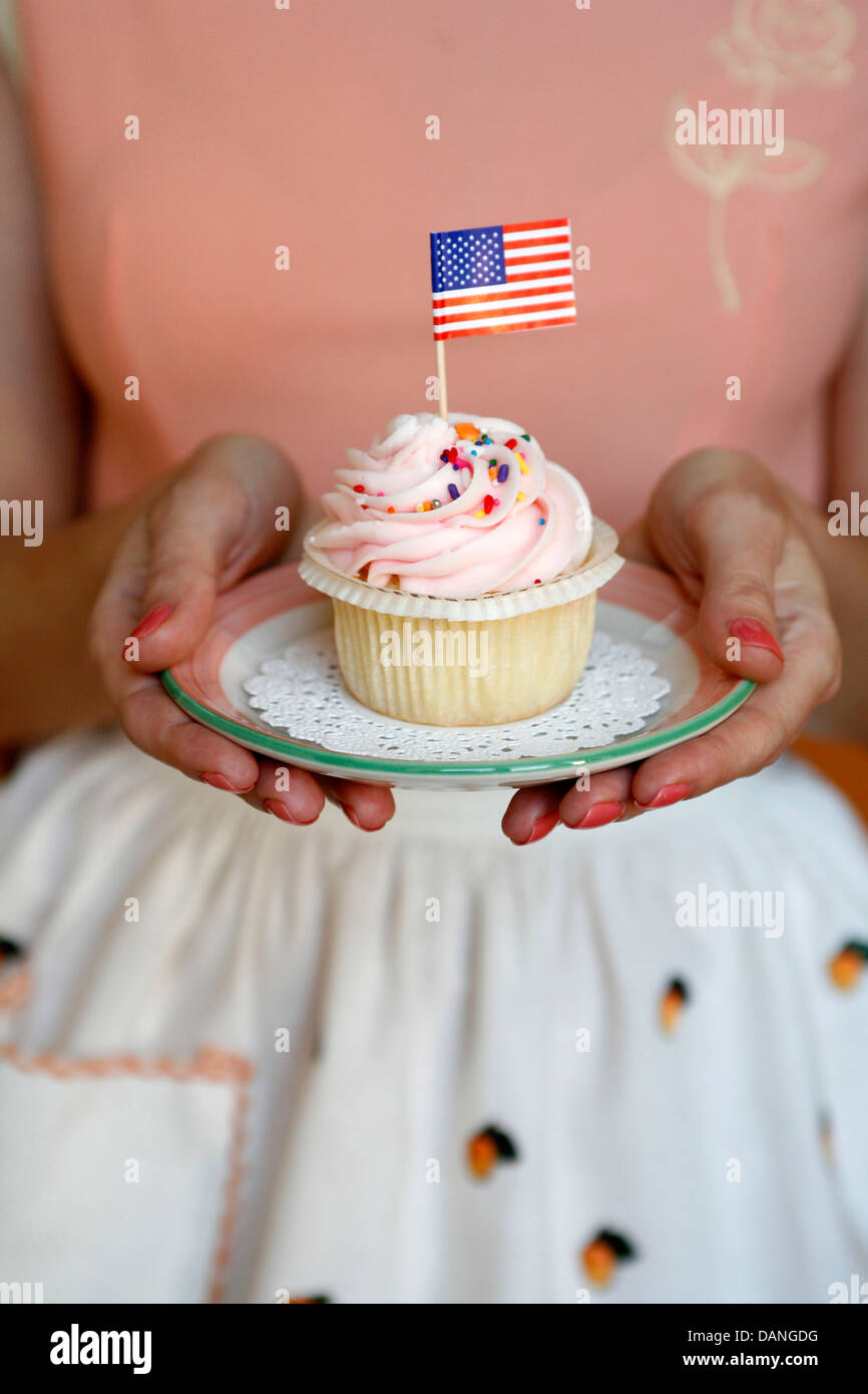 Gastgeberin bietet einen bunten Cupcake mit einer amerikanischen Flagge drin. Stockfoto