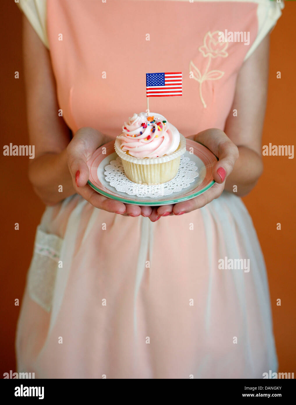 Gastgeberin bietet einen bunten Cupcake mit einer amerikanischen Flagge drin. Stockfoto