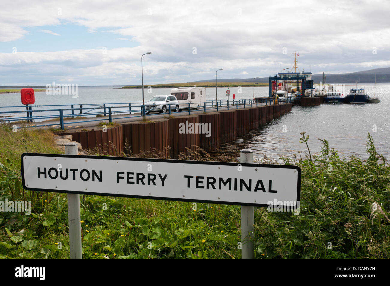 Zeichen für Houton Ferry Terminal auf Orkney Festland mit Fahrzeugen, die Fähre verlassen, im Hintergrund. Stockfoto