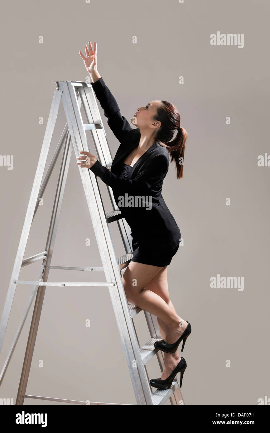 Chinesische Geschäftsfrau trägt einen dunklen Anzug und eine Leiter klettern. Konzeptbild über Ehrgeiz und Erfolg. Stockfoto
