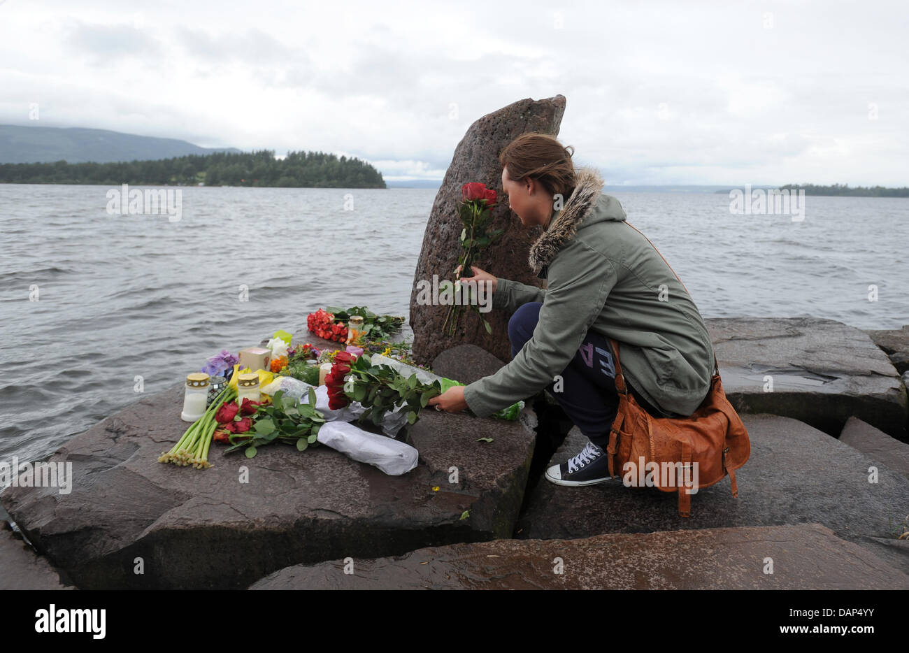 Eine Mädchen legt Blumen an einem improvisierten Denkmal für die Opfer des Massakers auf der Insel Utoya (Hintergrund), Utvika, Norwegen, 24. Juli 2011. Die Bombardierung der Regierungsgebäude in Oslo und der anschließenden Amoklauf in einem politischen Jugendcamp auf der Insel Utoya am 22. Juli 2011 haben mehr als 90 Leben behauptet. Foto: Britta Pedersen Dpa +++(c) Dpa - Bildfunk +++ Stockfoto