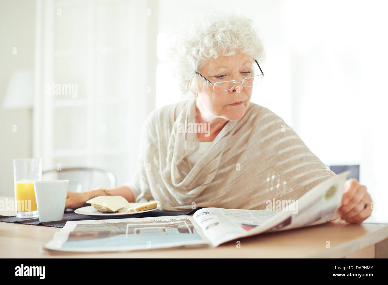 Entspannte senior Frau ihr frühstücken und die Morgennachrichten lesen Stockfoto