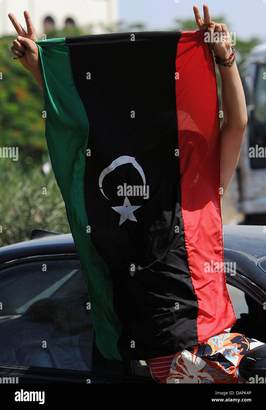 Ein Mann sitzt auf einem Autofenster und jubelt mit einer Flagge, wie er einen Kontrollpunkt der Rebellen in Tripolis, Libyen, 24. August 2011 geht. Viele Menschen fliehen aus der Schlacht in der Stadt. Obwohl das Gaddafi-Regime in der Nähe von Zusammenbruch, Kämpfe zwischen den Gaddafi-Loyalisten und rebellischen Kräfte noch weiter ist. Foto: Hannibal Stockfoto