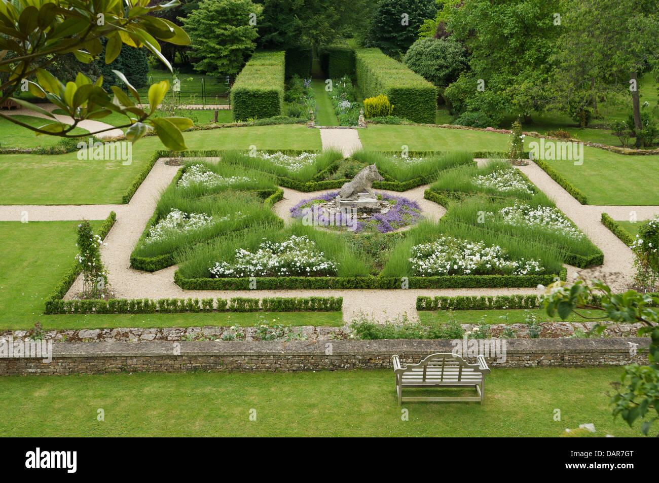 Box Hedge-Grenzen und Wege im Garten mit Stein Schwein Statue im 17. Jahrhundert englisches Landhaus Ampney Park Stockfoto