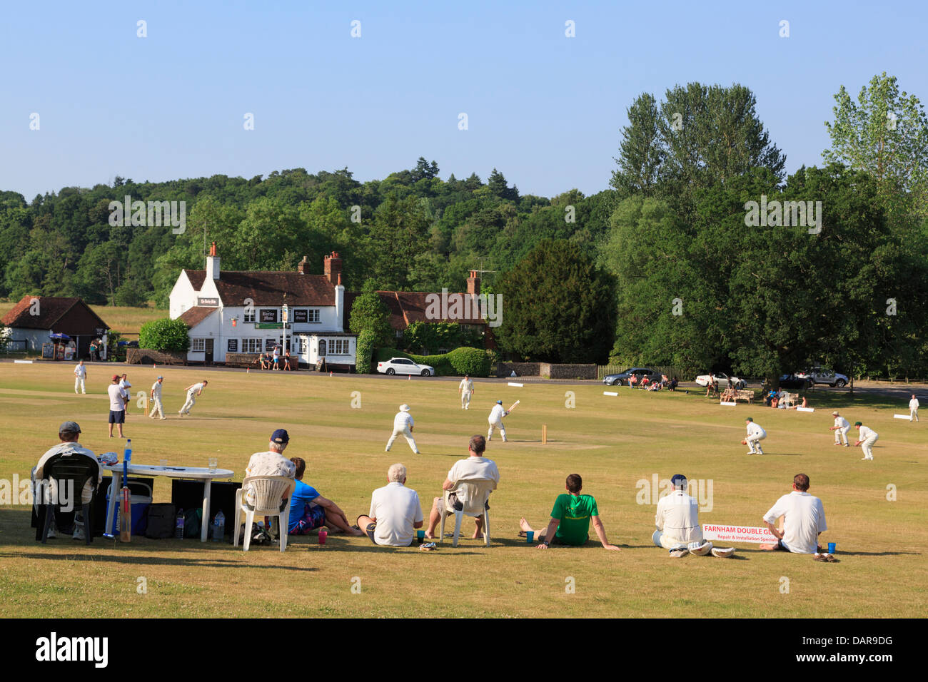 Lokale Team spielen Cricket Match auf Village Green vor der Gerste Mähen Pub an einem Sommerabend. Tilford Surrey England Großbritannien Großbritannien Stockfoto