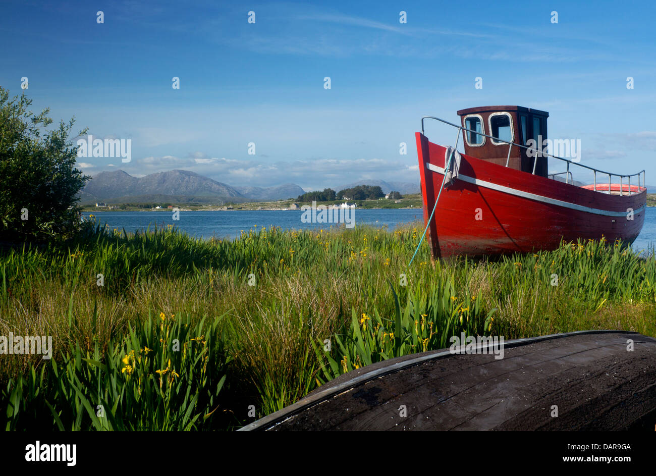 Roten Fischerboot am Ufer der Mündung Roundstone Connemara einige der zwölf Pins / Twelve Bens im Hintergrund Co Galway Irland Stockfoto