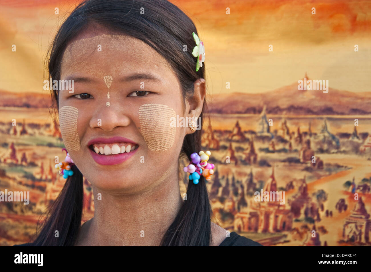 Junge Frau mit Thanaka-Rinde Make-up mit Malerei von Pagoden in Bagan-Ebene im Hintergrund. Stockfoto