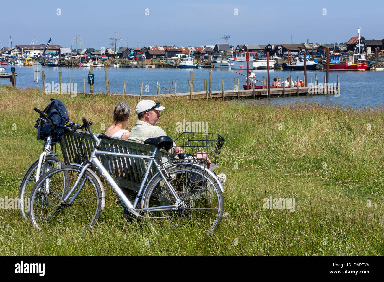 Ein paar Radfahrer machen Sie eine Pause auf einer Bank mit Blick auf die Mündung bei Blackshore in der Nähe von Walberswick in Suffolk - England. Stockfoto