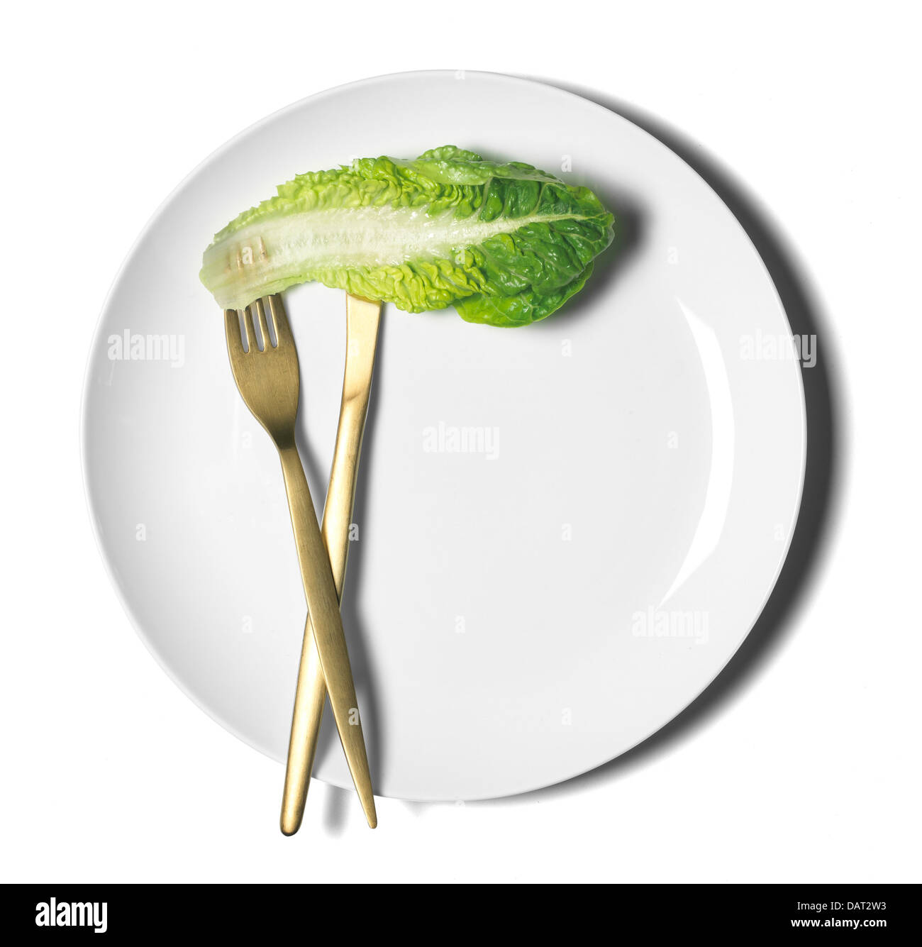 weißer Teller mit Messer und Gabel und einzelnes Salatblatt ausgeschnitten auf weißem Hintergrund Stockfoto