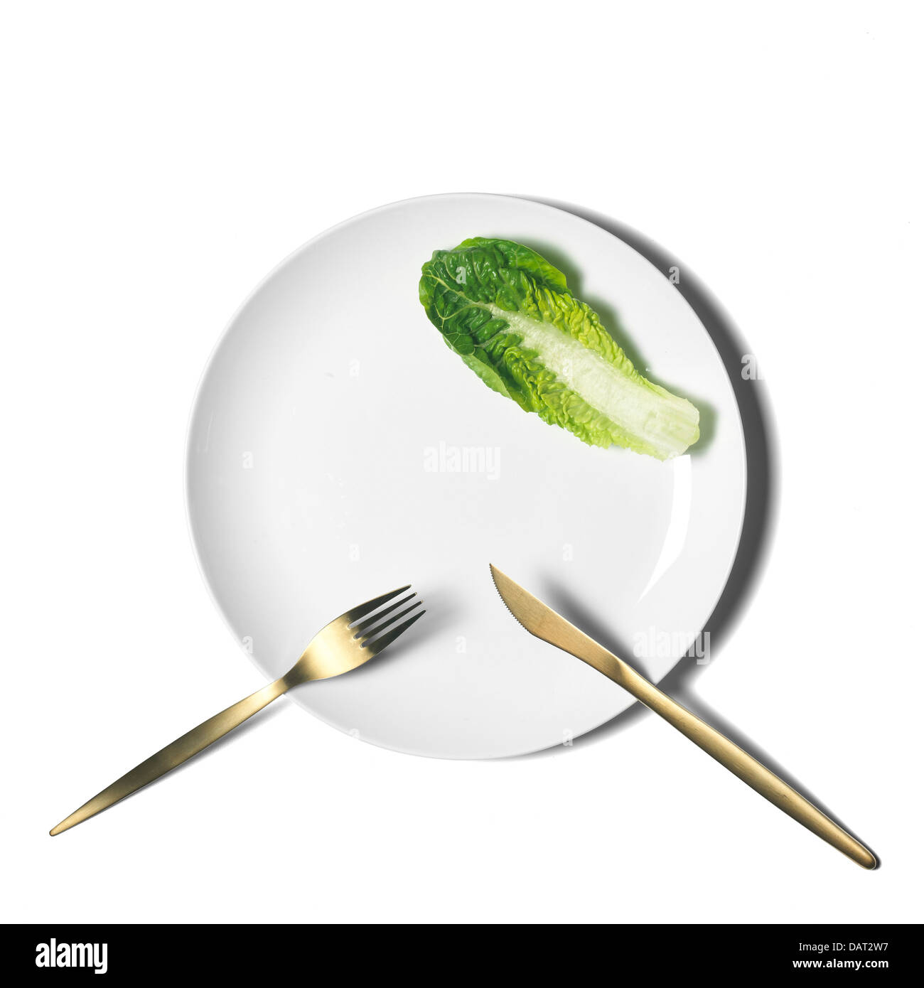 weißer Teller mit Messer und Gabel und einzelnes Salatblatt ausgeschnitten auf weißem Hintergrund Stockfoto