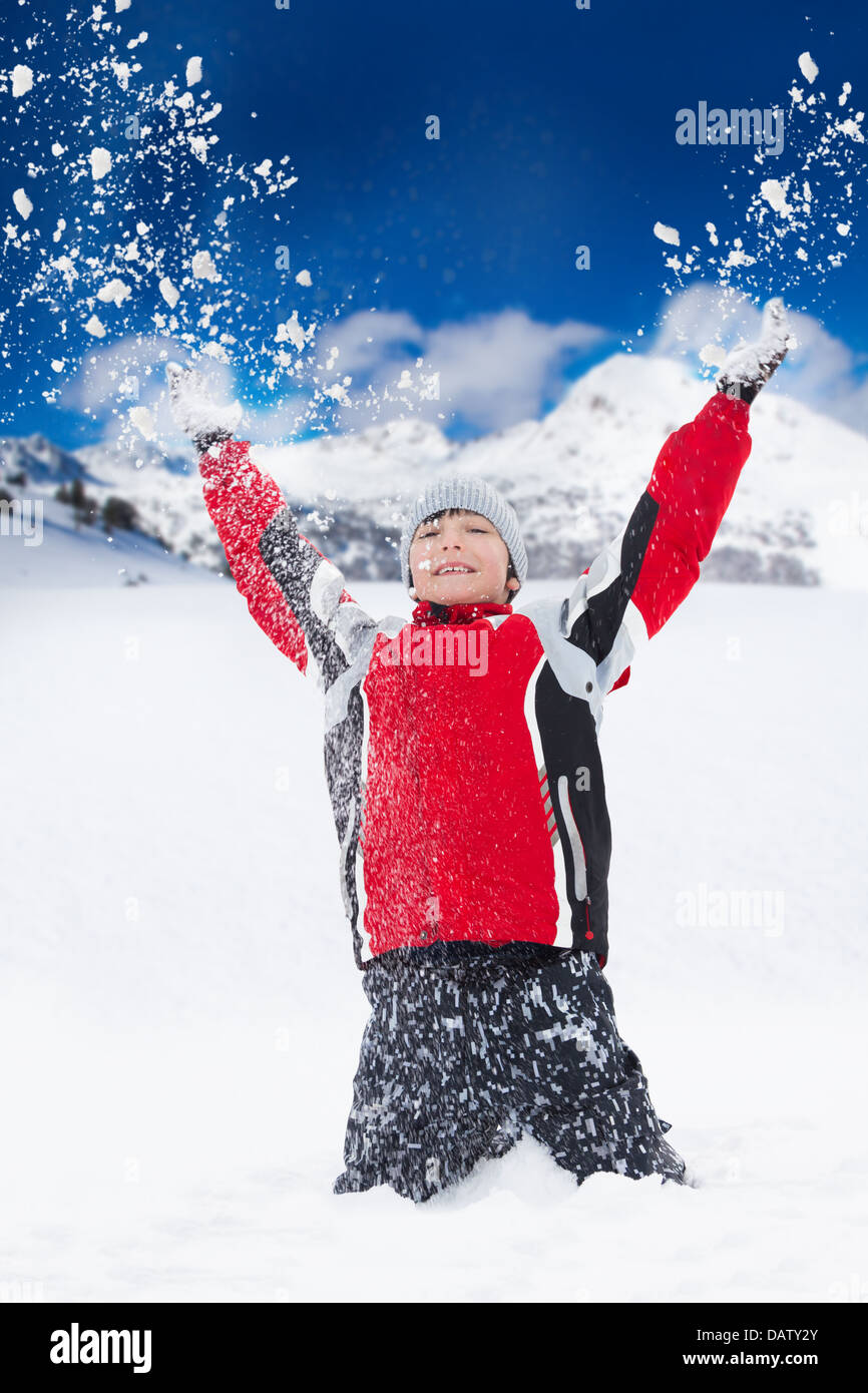 Glücklicher lächelnder junge wirft Schnee in der Luft mit Schneeflocken fliegen in alle Richtungen Stockfoto
