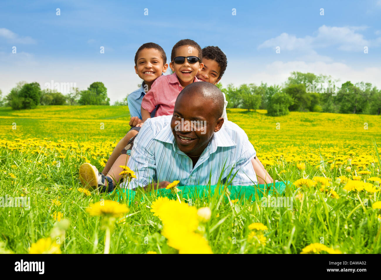 Glücklich lächelnd schwarze Afrikaner mit jungen sitzt auf seinem Rücken legen im Frühjahr Park Bereich mit gelben Löwenzahn Stockfoto