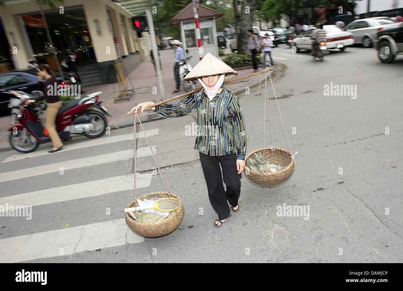 Eine Frau, die einen traditionellen Hut überquert die Straße mit einem herkömmlichen Gerät für den Transport von Gütern, zwei Körbe auf einem Stick in Hanoi, Deutschland, Dienstag, 27. März 2007.  Foto: Peter Kneffel Stockfoto