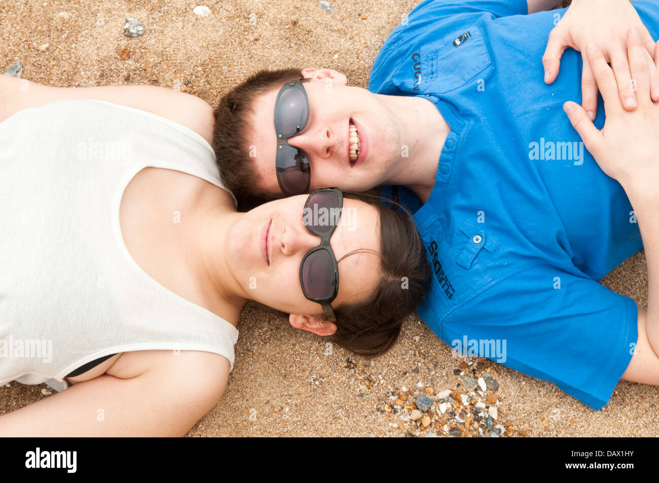 Ein junges Paar in ihren späten Teens oder in frühen zwanziger Jahren Sonnenbrille verlegen den Kopf an einem Strand Stockfoto