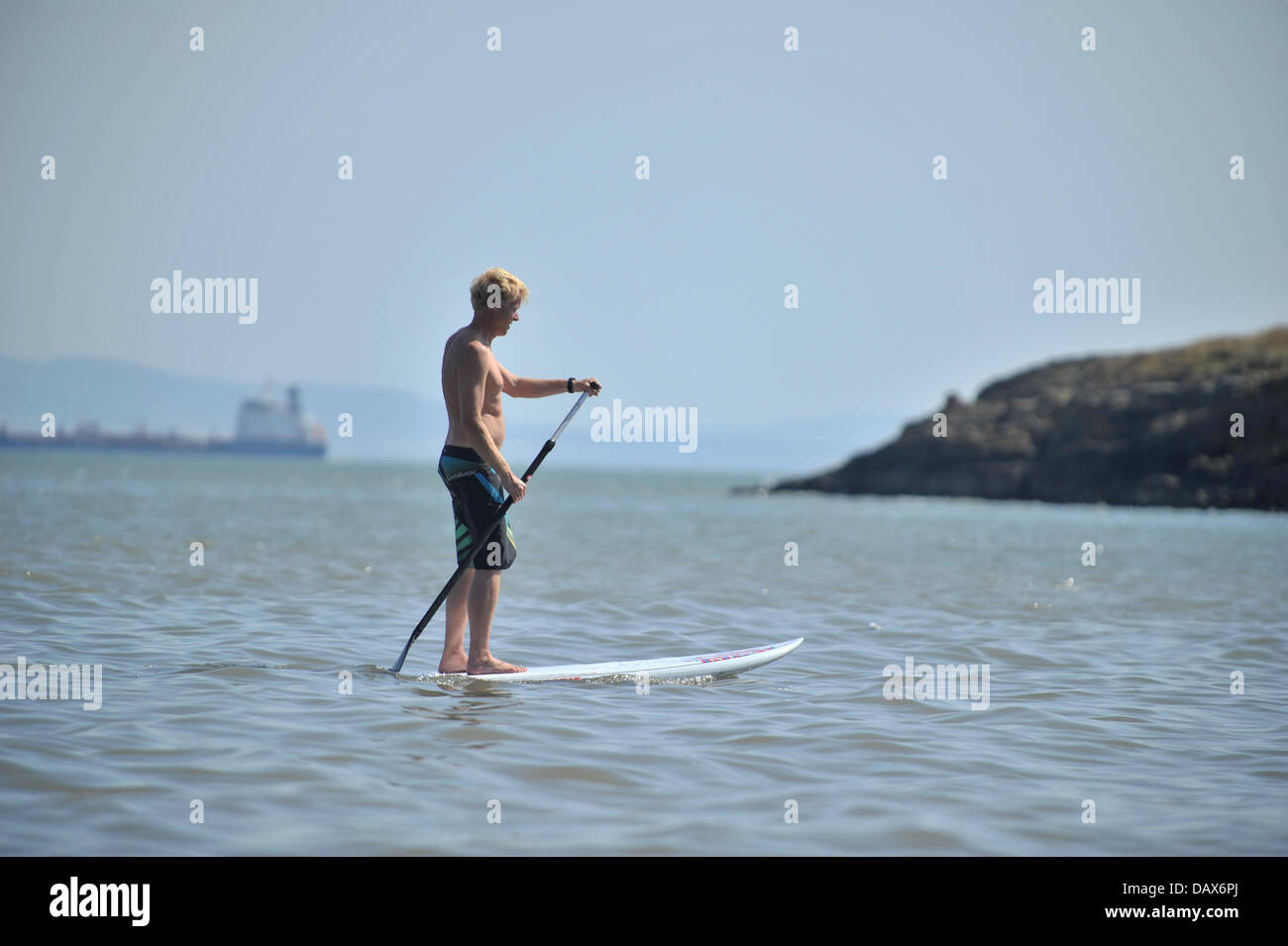 BARRY ISLAND, VEREINIGTES KÖNIGREICH. 19. Juli 2013. Die britische Hitzewelle weiter und die Menschen strömen zu den Stränden in Süd-Wales. Ein Mann Paddel durch das Wasser stehend auf einem Surfbrett. Foto Credit: Polly Thomas / Alamy Live News Stockfoto