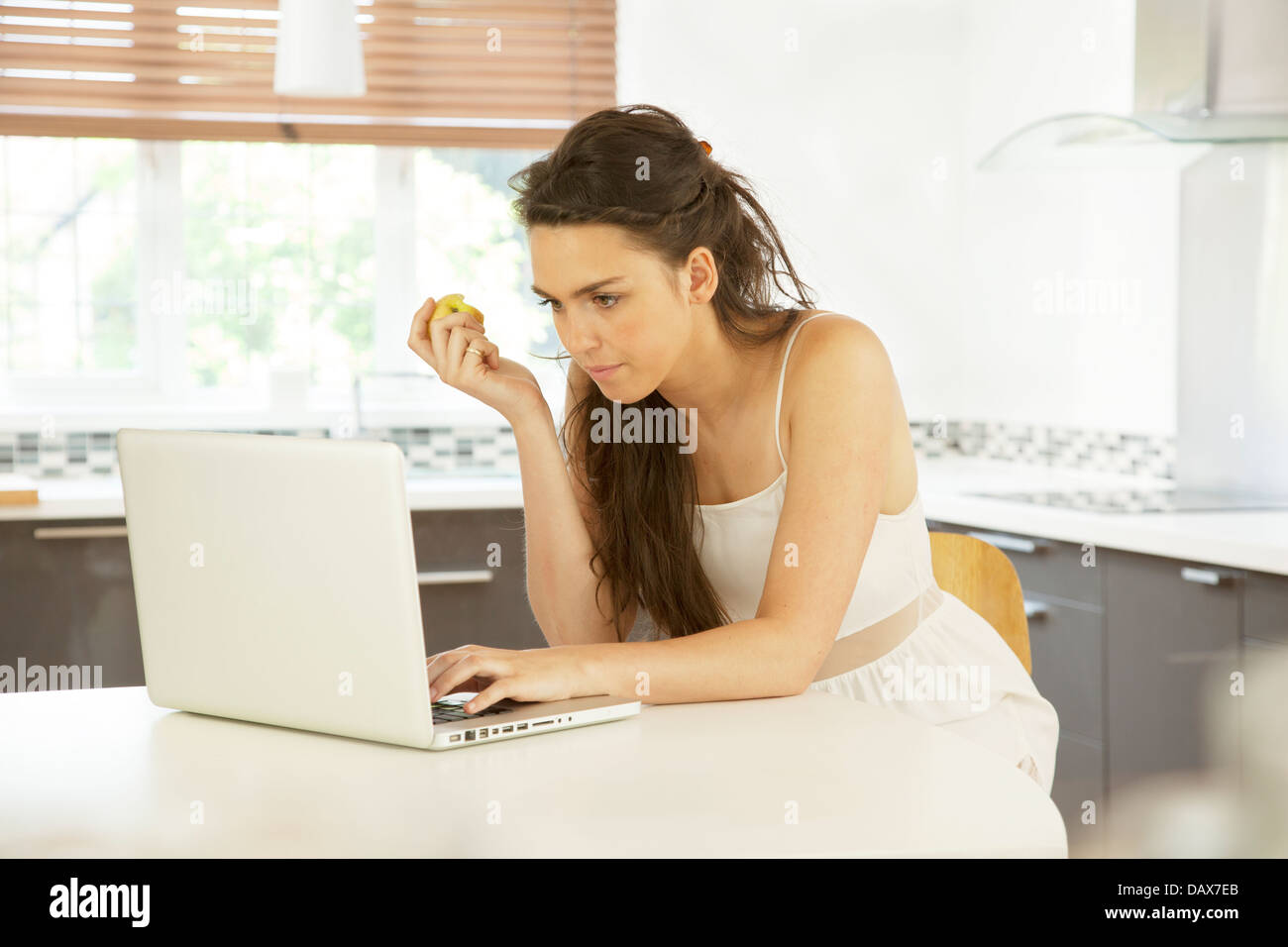 Junge Frau in einer Küche mit einem Laptop hält einen Apfel. Stockfoto