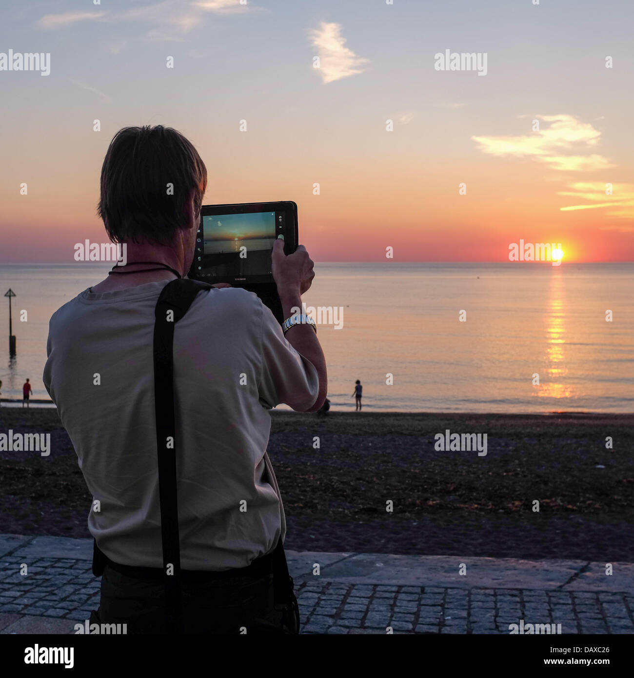 Aberystwyth Ceredigion, Wales, UK, Mann Freitag, 19. Juli 2013 den Sonnenuntergang auf einem Tabletcomputer an der Promenade und Strand an der Aberystwyth Wales UK zu fotografieren.   Mit Temperaturen bis zu fast 30c und ein heißer, trockener Wind aus dem Land wurde die Westküste von Wales berichtet, die heißesten Teil des Vereinigten Königreichs auf Freitag, 19. Juli 2013. Wassertemperaturen wurden aufgenommen von über 18 Grad Celsius vor der Küste und sogar wärmer auf dem flachen Gewässer in der Nähe der Strände. Bildnachweis: Keith Morris/Alamy Live-Nachrichten Stockfoto