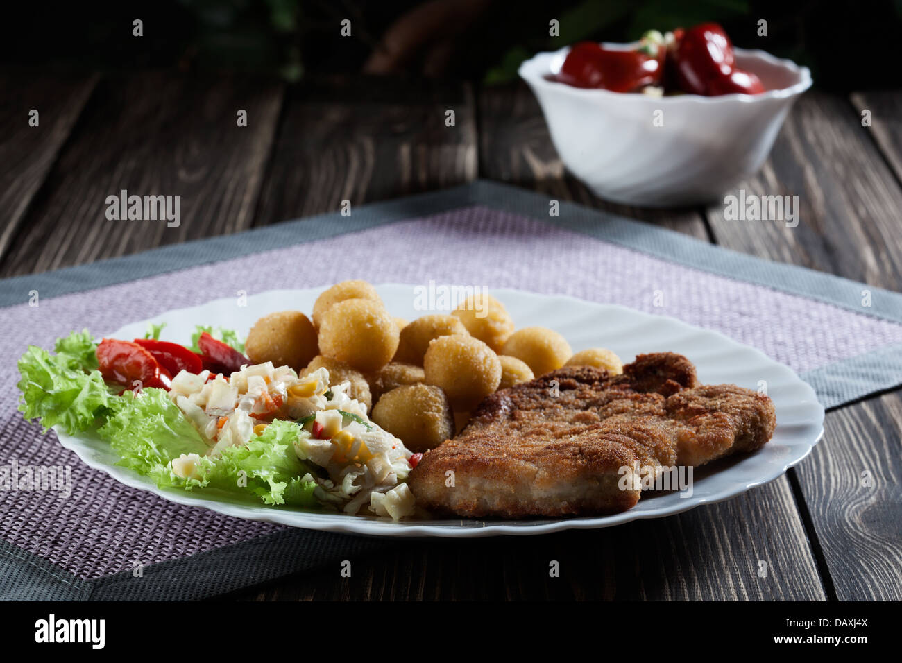 Paniertes Kotelett, Kartoffeln und Salat zubereitet. Geheimnisvolles Licht Stockfoto