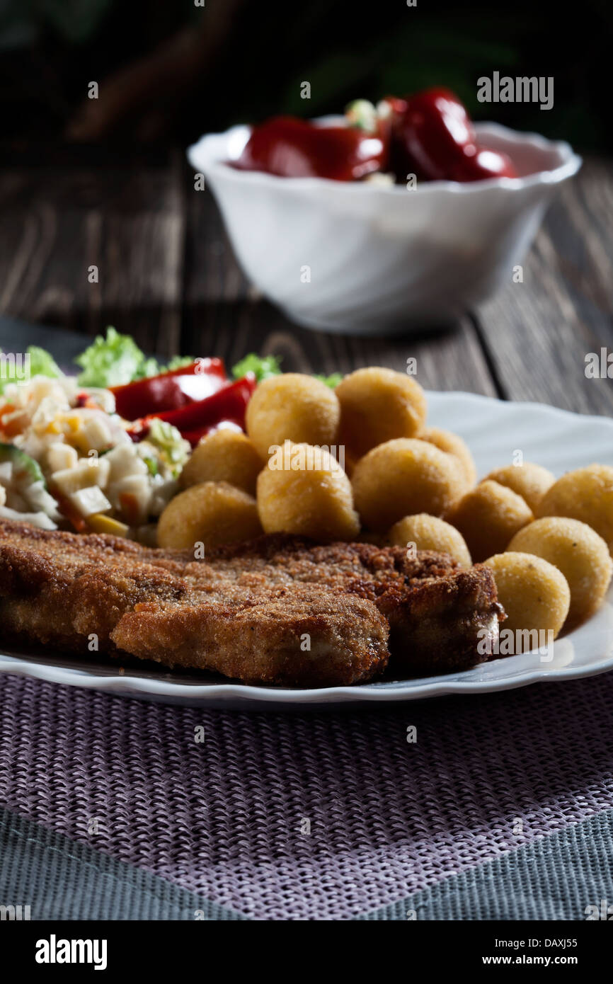 Paniertes Kotelett, Kartoffeln und Salat zubereitet. Geheimnisvolles Licht Stockfoto