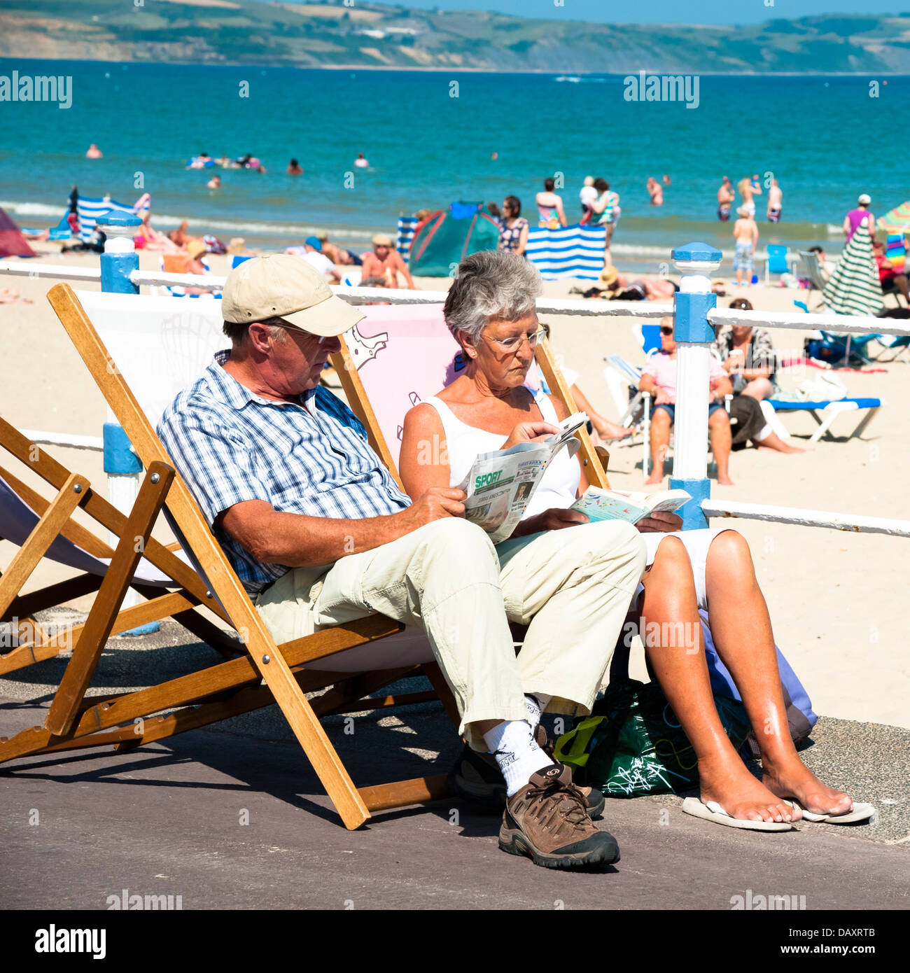 Paar, sitzen in Liegestühlen am Strand von Weymouth, Dorset, UK lesen. Stockfoto