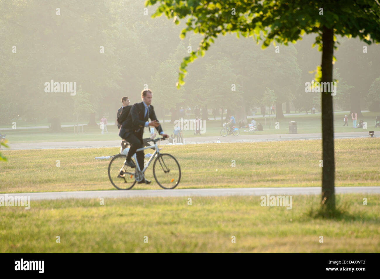 jungen männlichen Erwachsenen in Business-Anzug mit dem Rad zur Arbeit durch Kensington Gardens Park London Blick auf sein Handy Fahrrad Stockfoto