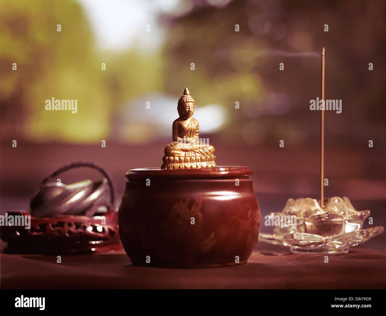 Kleine Statue des Meditierenden Buddha, Rauchen, Räucherstäbchen und buddhistischen Tingsha Glockenspiel Glocken künstlerischen Stillleben Stockfoto