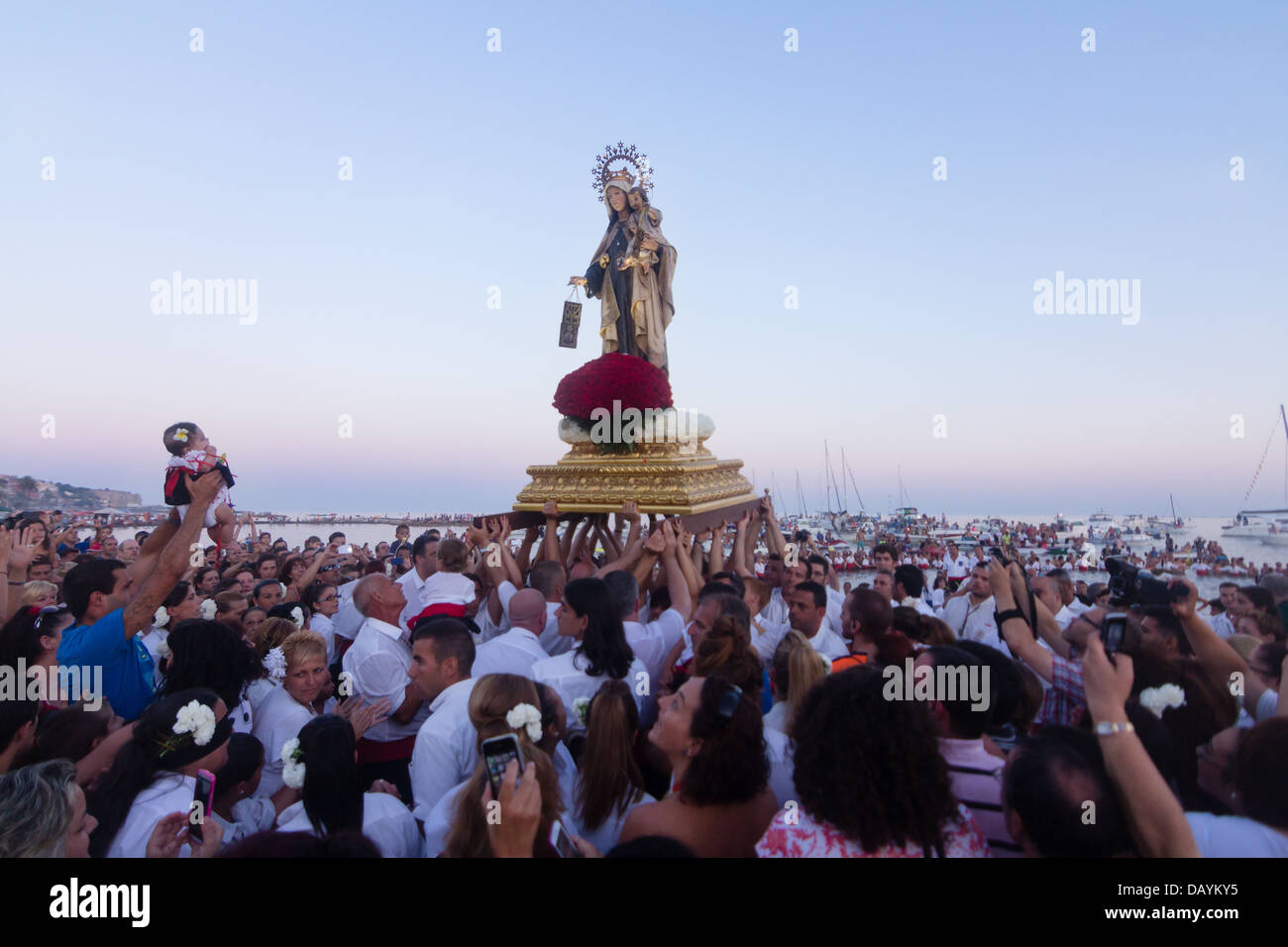 Nicht identifizierte lokale Verehrer heben seine Tochter vor einem religiösen Bild am Strand während des Festivals der Virgen del Carmen Stockfoto