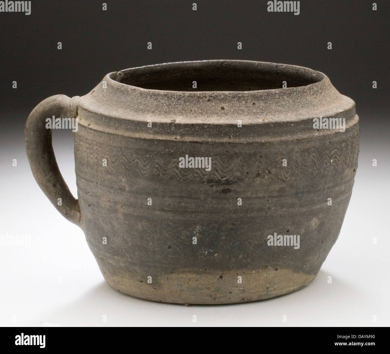 Dieses Gefäß mit Griff ist ein funktionales Kunstwerk aus Keramik. Es zeigt die Einfachheit und Zweckmäßigkeit von alten Töpferdesigns, wobei der Schwerpunkt auf Gebrauchsgegenstand und Handwerkskunst liegt. Die Form und Struktur des Glases unterstreichen seine historische und kulturelle Bedeutung. Stockfoto