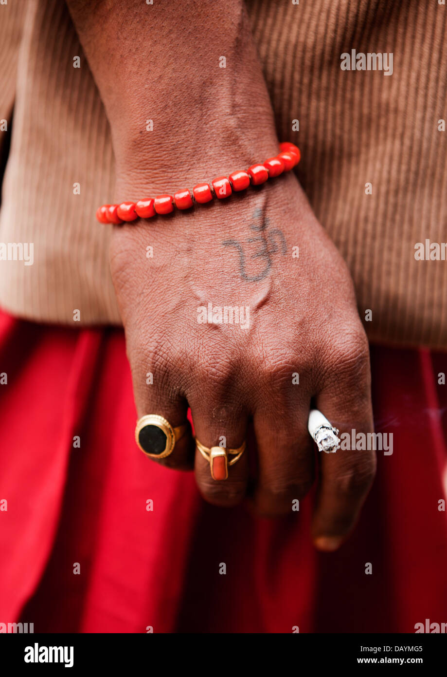 Ein Pilger auf der Maha Kumbh Mela in Indien hält eine Zigarette in der Hand der Aum tätowiert. Stockfoto
