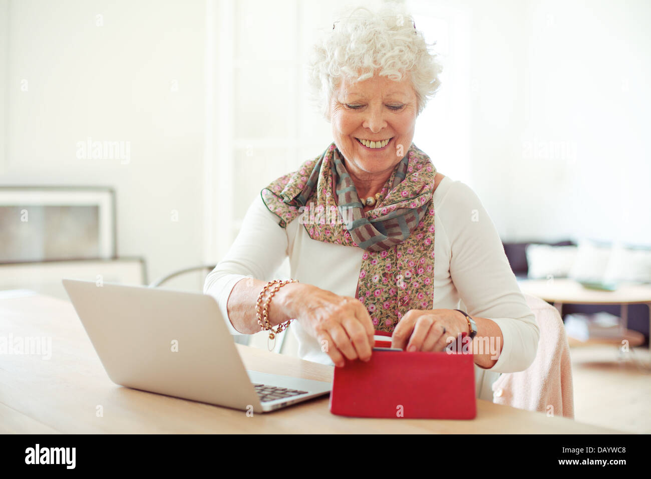Fröhliche alte Frau vor Laptop immer etwas aus ihrer Brieftasche Stockfoto