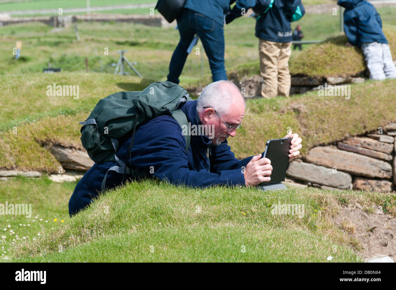 Ein Tourist, der einen Tablet-Computer als Digitalkamera verwendet, um ein Foto bei Skara Brae zu machen. Senior mit moderner Technologie. Stockfoto