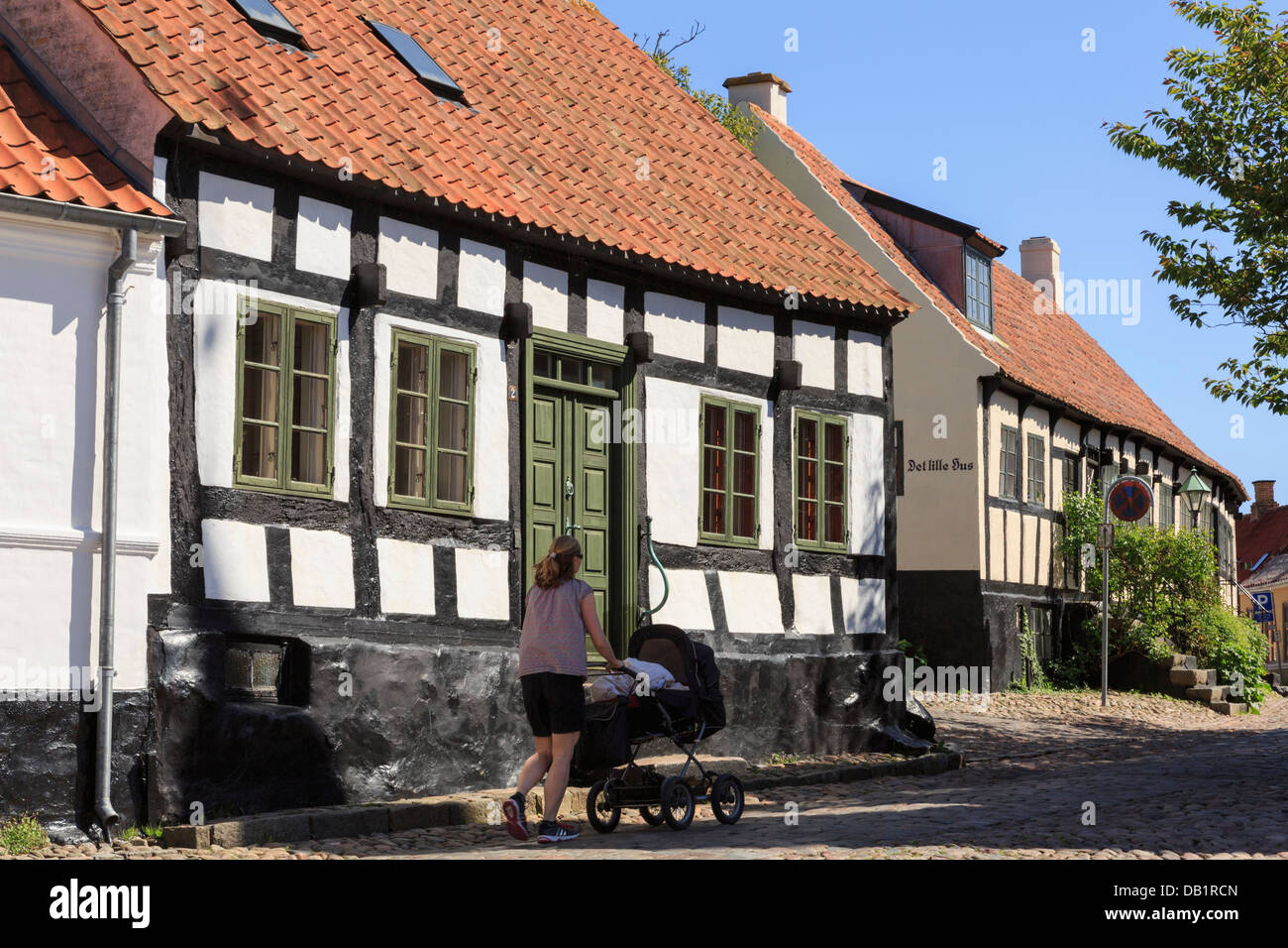 Frau schob einen Kinderwagen über Kopfsteinpflaster vorbei an malerischen alten Häusern auf schmalen gepflasterten Straße Overgade, Ebeltoft, Jütland, Dänemark Stockfoto