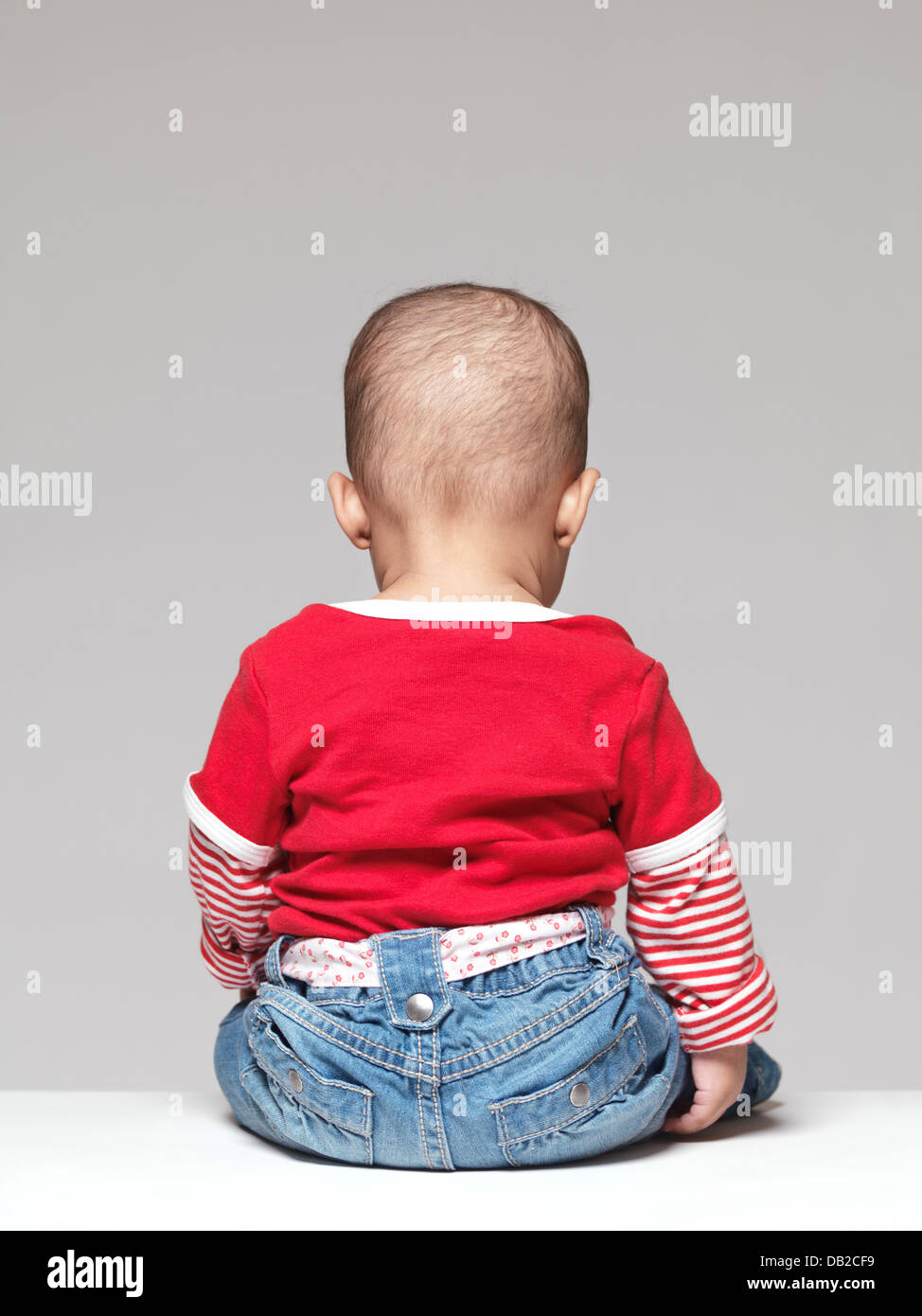 Baby sitzt mit dem Rücken zur Kamera auf grauem Hintergrund isoliert Stockfoto